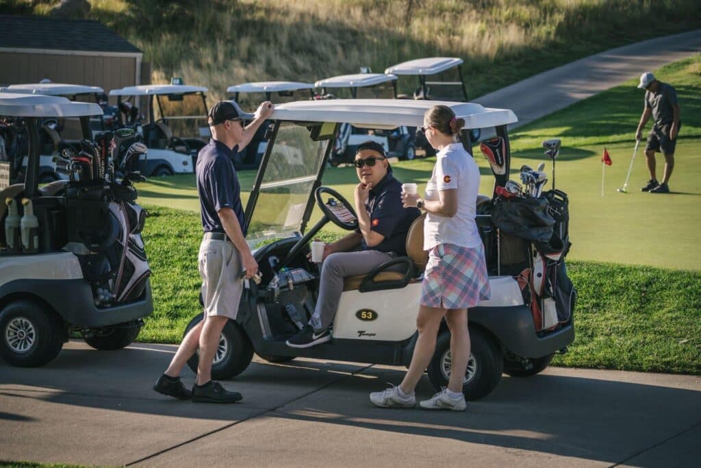 Three golfers, one in golf car, connecting and building relationships during a charity tournament.