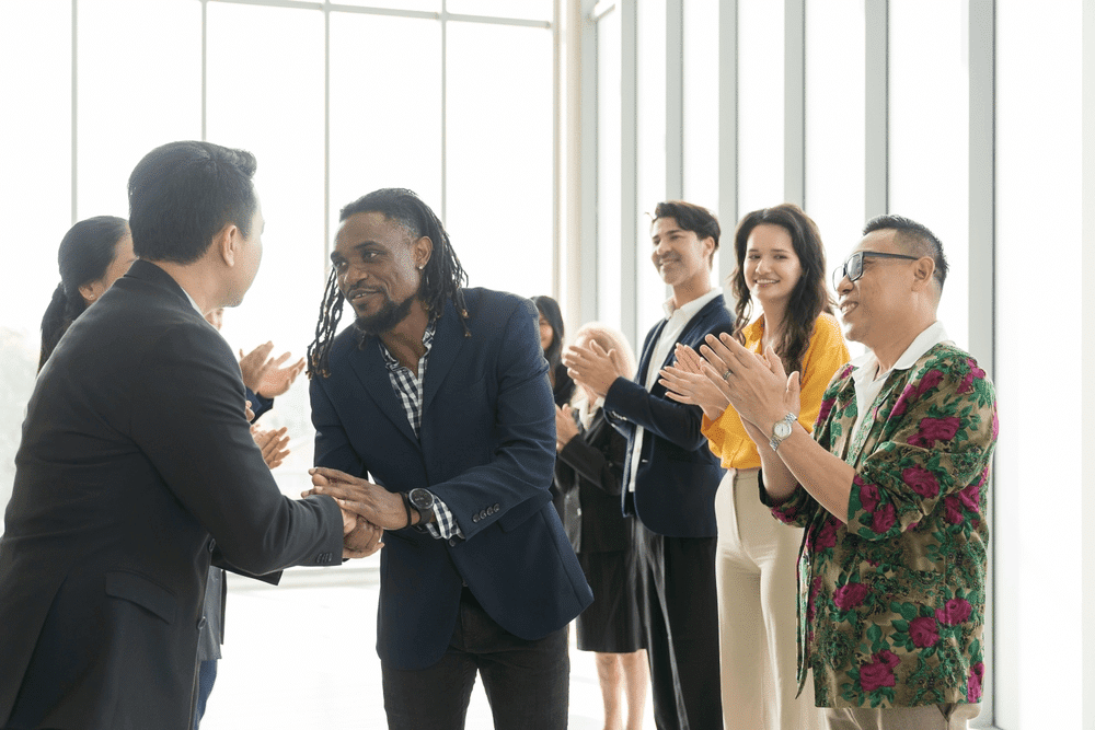 Colleagues smiling and clapping in a bright office corridor, illustrating a successful partnership agreement for nonprofit event sponsorships.