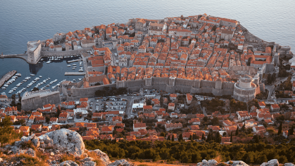 Aerial view of Dubrovnik Old Town in Croatia, showing its historic stone city walls, red-tiled rooftops and Adriatic coastline.