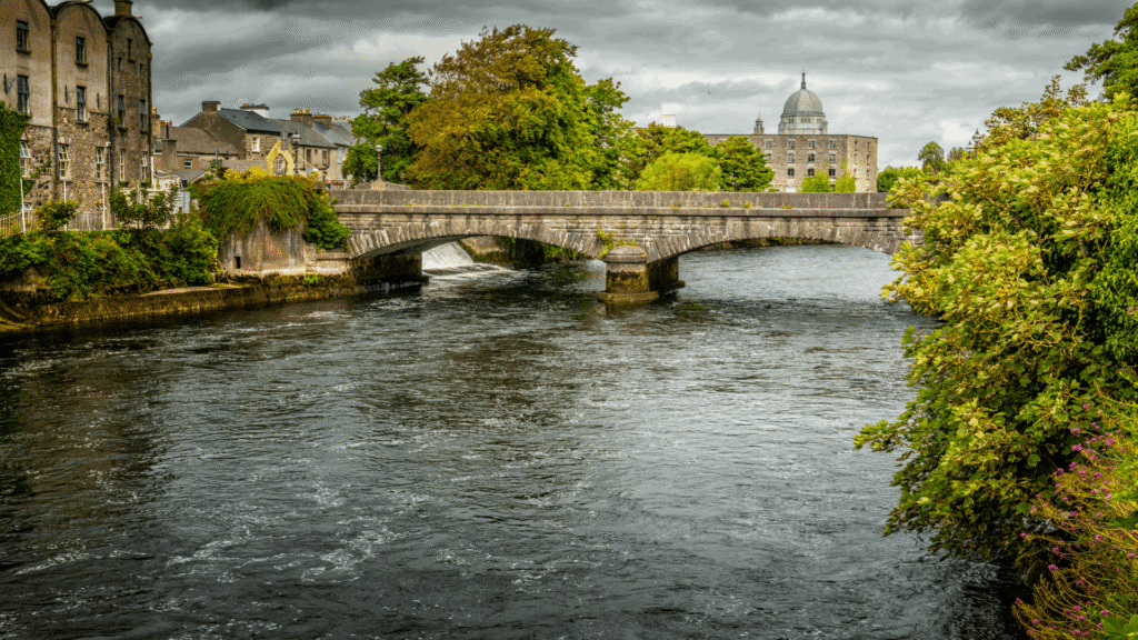 River Corrib flowing beneath a stone bridge with Galway city landmarks in the background