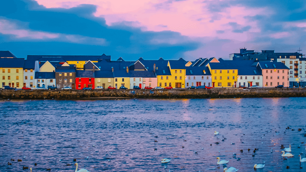 Colorful waterfront buildings along the river in Galway, Ireland, beneath dramatic coastal clouds