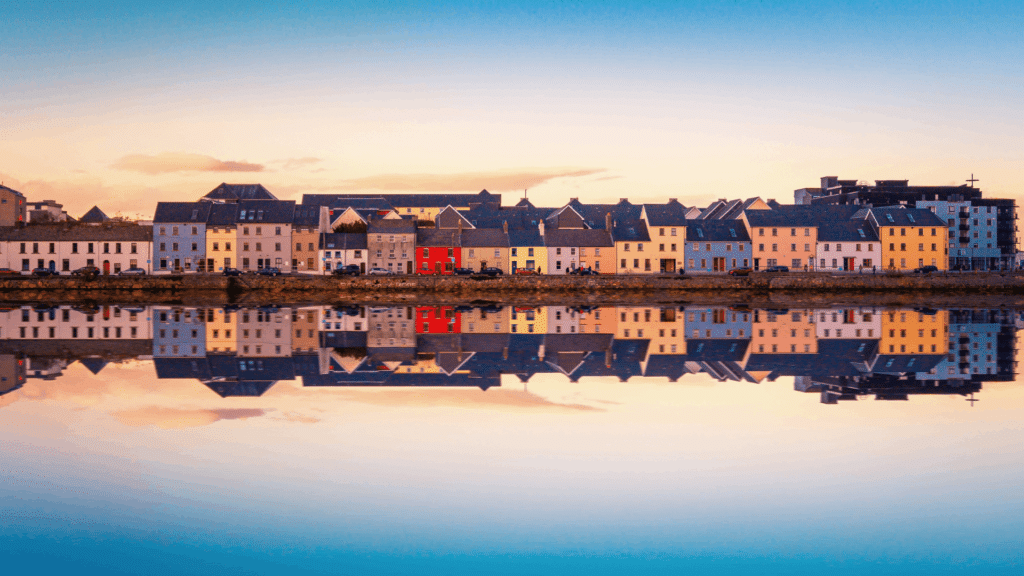 Colorful houses reflected in calm water along the Galway waterfront at sunset